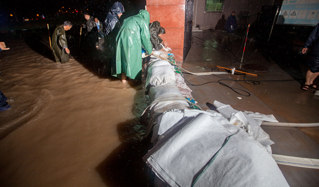 图为7月19日，河南滑县电力员工在110千伏文明变电站外顶着暴雨进行防涝作业。