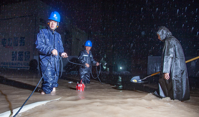 图为7月19日，河南滑县电力员工在110千伏文明变电站外顶着暴雨进行防涝作业。