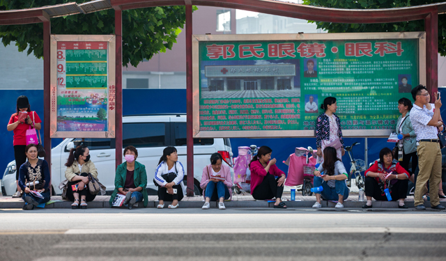 图为6月7日，学校门前的的一个公交车站点，下面坐满了考生家长，有低头看书、看手机的，有带着口罩想事的，气氛紧张的胜过考生。