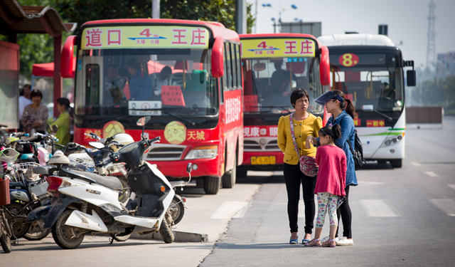 图为6月7日，接送考生的公交专用车前，两名妇女带着小女儿在议论考点里孩子考试成绩的事。
